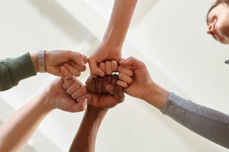 Four diverse team members join fists together, displaying unity and teamwork.